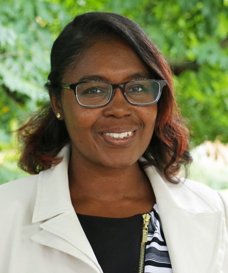 Professional of a black woman, smiling, with glasses. Ironically, there are trees in the background. She hopes to one day replace this photo with something water-themed